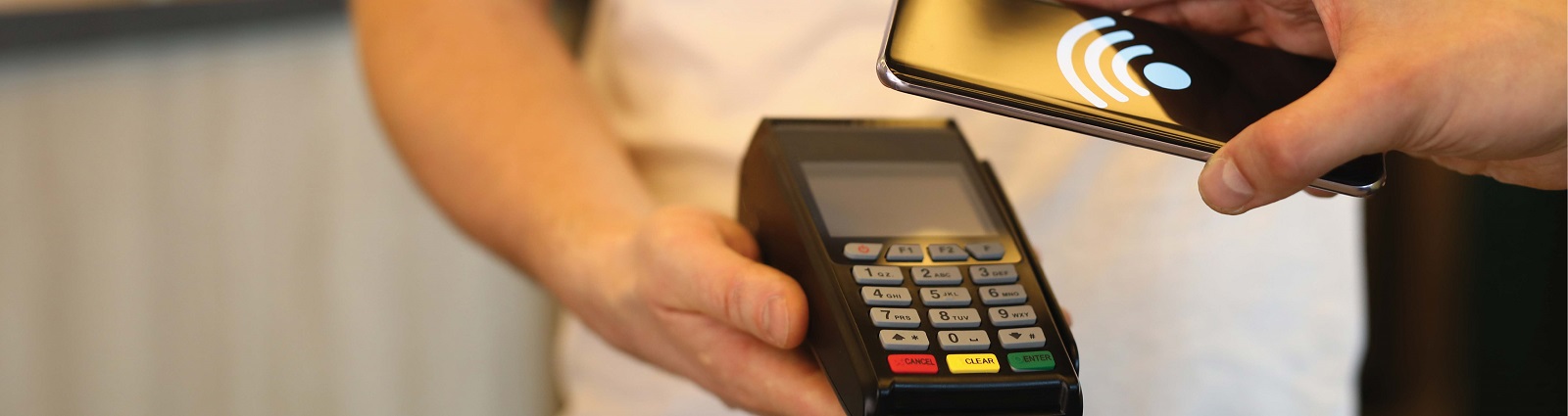 Person using their mobile phone to make a transaction through a point of sale terminal.