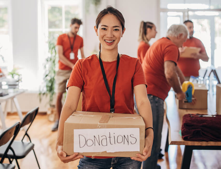 A woman smiling and looking at the camera while holding a box labeled "Donations"