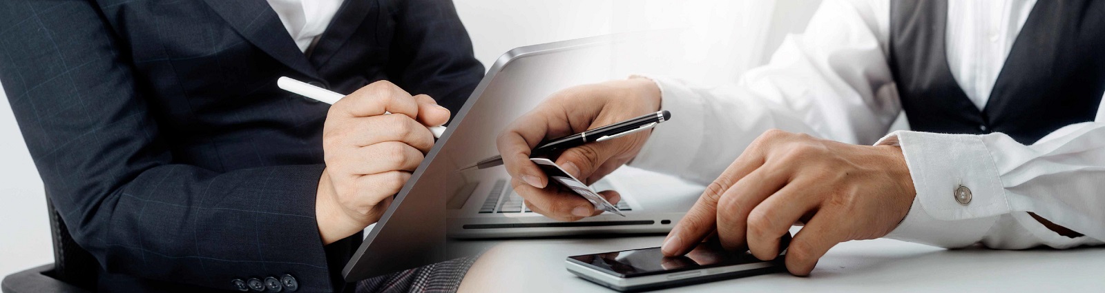 Two people in business attire, one holding a credit card, and the other one using their tablet.