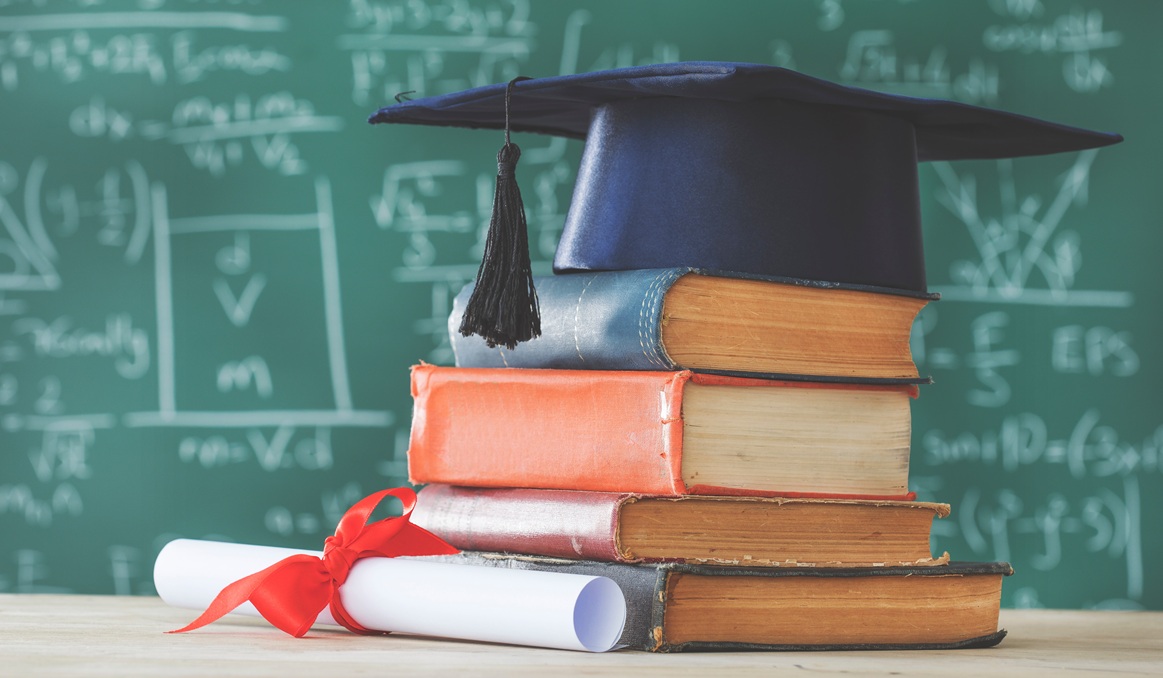 Stack books graduate hat and diploma in front of green chalkboard